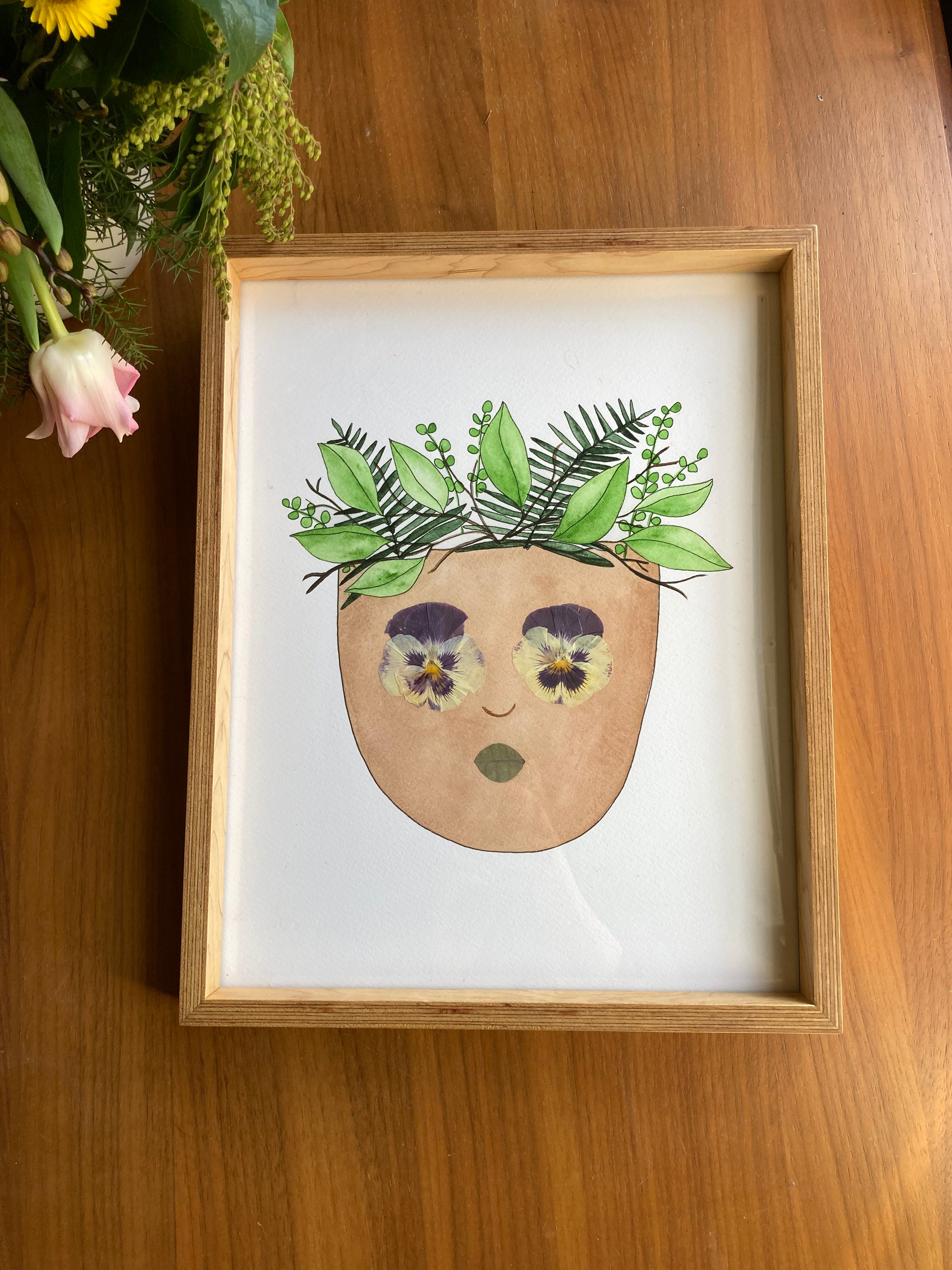 Watercolor light skinned face with plants for hair. Real pressed pansy eyes and green eucalyptus lips.